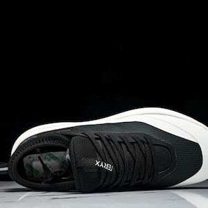 May include: Black and white athletic shoe with the word "TERYX" on the side. The shoe has a black upper with white accents and a white sole. The shoe is lying on its side against a black background.