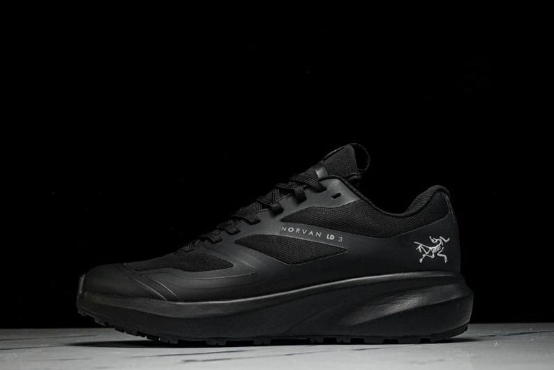 May include: Black athletic shoe with the text "NORVAN LD 3" and a logo on the side. The shoe has a thick sole and a mesh upper. The shoe is designed for running and outdoor activities.