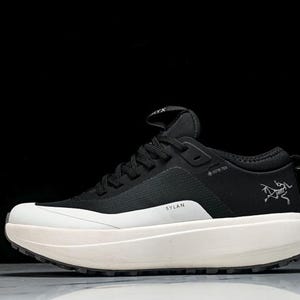 May include: Black and white athletic shoe with a thick, off-white sole. The shoe features the text "SYLAN" and a logo on the side. The shoe has black laces and a pull tab at the heel.