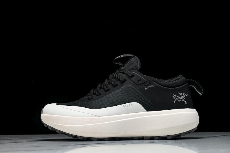 May include: Black and white athletic shoe with a thick, off-white sole. The shoe features the text "SYLAN" and a logo on the side. The shoe has black laces and a pull tab at the heel.