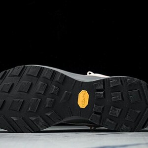 May include: Close-up of the sole of a beige and black athletic shoe. The black sole has a textured pattern with a yellow "Vibram" logo. The shoe is designed for outdoor activities.