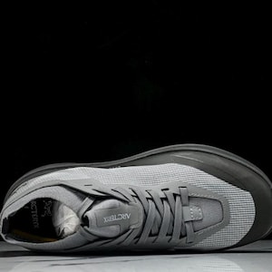 Puede incluir: Zapatilla deportiva gris con una parte superior de malla y una suela gris oscuro. El zapato tiene un cierre de cordones y la marca "Arc'teryx" es visible en la leng&uuml;eta. Dise&ntilde;ado para correr u otras actividades deportivas.
