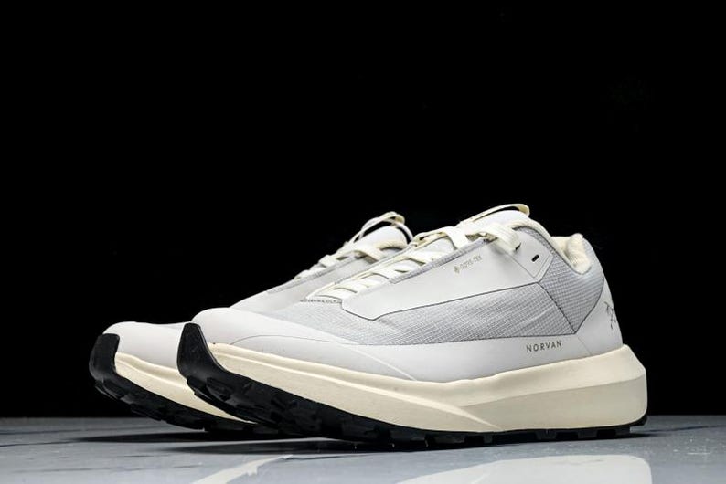 May include: Pair of light gray athletic shoes with black soles. The shoes have a textured upper and a thick, off-white midsole. The word "NORVAN" is printed on the side. The shoes are designed for outdoor activities.