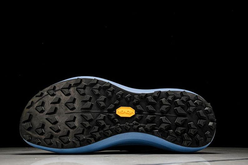 May include: Close-up of the sole of a running shoe. The sole is black with a textured pattern and a light blue midsole. A yellow "Vibram" logo is visible.