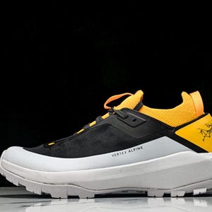 Puede incluir: Zapatilla deportiva negra y amarilla con suela blanca. La zapatilla tiene una parte superior negra con detalles amarillos en el tal&oacute;n y la leng&uuml;eta. Las palabras "VERTEX ALPINE" est&aacute;n impresas en el lateral.