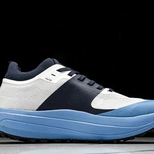 May include: A modern athletic shoe with a light blue sole and a white and navy blue upper. The shoe features a mesh-like material and a thick sole. The word "HAUX" is printed on the side of the shoe.
