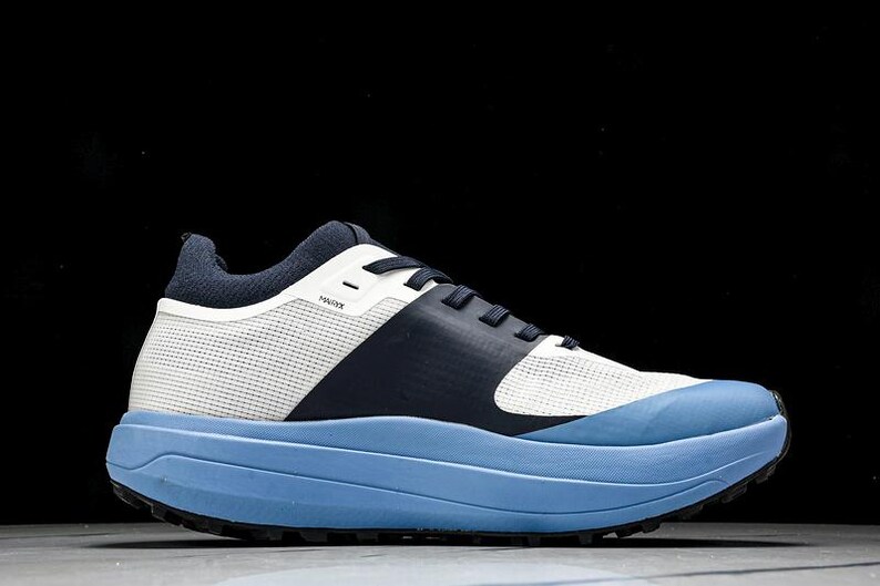 May include: A modern athletic shoe with a light blue sole and a white and navy blue upper. The shoe features a mesh-like material and a thick sole. The word "HAUX" is printed on the side of the shoe.