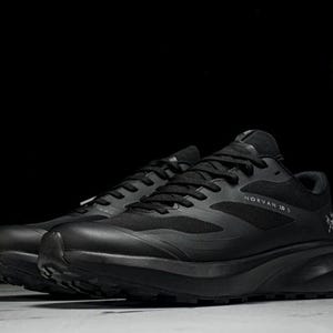 May include: Pair of black athletic shoes with the text "NORVAN IS" on the side. The shoes have a mesh upper, black laces, and a thick, textured sole. The shoes are designed for running or trail activities.