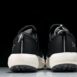 May include: Pair of black and white athletic shoes, viewed from the back. The shoes have a black upper with white soles and a textured, dark gray outsole. A reflective stripe runs down the heel.