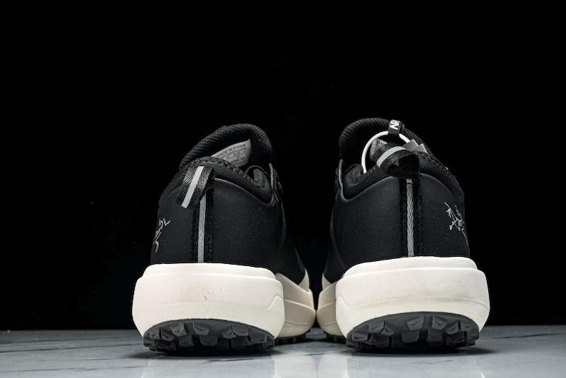 May include: Pair of black and white athletic shoes, viewed from the back. The shoes have a black upper with white soles and a textured, dark gray outsole. A reflective stripe runs down the heel.
