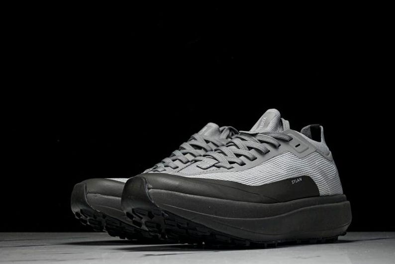 Puede incluir: Zapatillas deportivas grises con suelas negras. Las zapatillas tienen una parte superior texturizada y suelas gruesas. La palabra "STLAN" est&aacute; impresa en el lateral. Dise&ntilde;adas para correr u otras actividades deportivas.