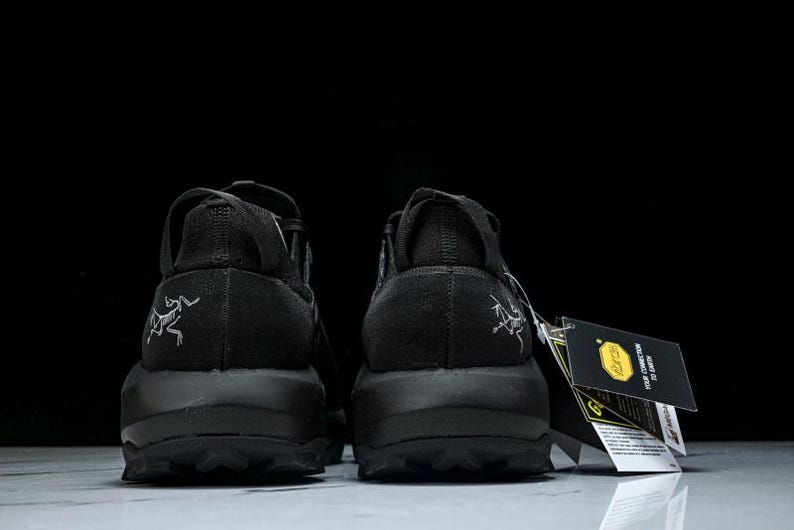 Puede incluir: Un par de zapatillas deportivas negras, vistas desde atr&aacute;s, con suela texturizada y un logotipo en el tal&oacute;n. Las zapatillas tienen una etiqueta con texto y un logotipo amarillo.