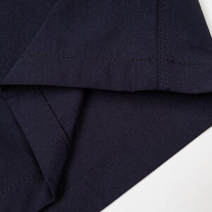 May include: Close-up of a section of navy blue fabric, showing the folded hem and stitching. The fabric has a subtle texture, and the stitching is visible along the edges, highlighting the garment's construction.