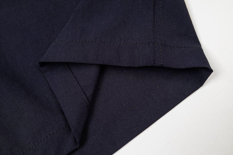 May include: Close-up of a section of navy blue fabric, showing the folded hem and stitching. The fabric has a subtle texture, and the stitching is visible along the edges, highlighting the garment's construction.