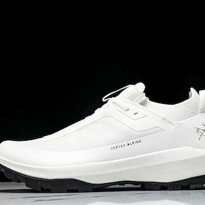 Puede incluir: Zapatilla deportiva blanca con suela negra. La zapatilla tiene el texto "VERTEX ALPINE" y un logotipo. Dise&ntilde;o aerodin&aacute;mico, probablemente para actividades al aire libre.