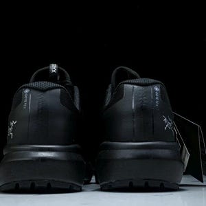 May include: A pair of black athletic shoes with a thick sole, viewed from the back. The shoes have the word "GORE-TEX" printed on the side and a logo. A tag hangs from one shoe.