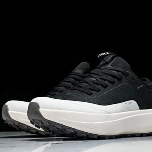 May include: Black and white athletic shoes with a thick, white sole. The shoes have black laces and a black upper with the word "STLAN" printed on the side. The brand name is visible on the tongue.
