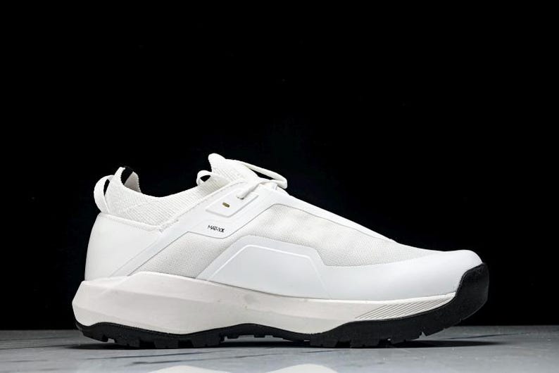 Puede incluir: Zapatilla deportiva blanca con suela negra. El calzado presenta un dise&ntilde;o aerodin&aacute;mico con una parte superior de malla y una suela gruesa y texturizada. Tiene una leng&uuml;eta en el tal&oacute;n y cierre de cordones. Dise&ntilde;ado para actividades deportivas.