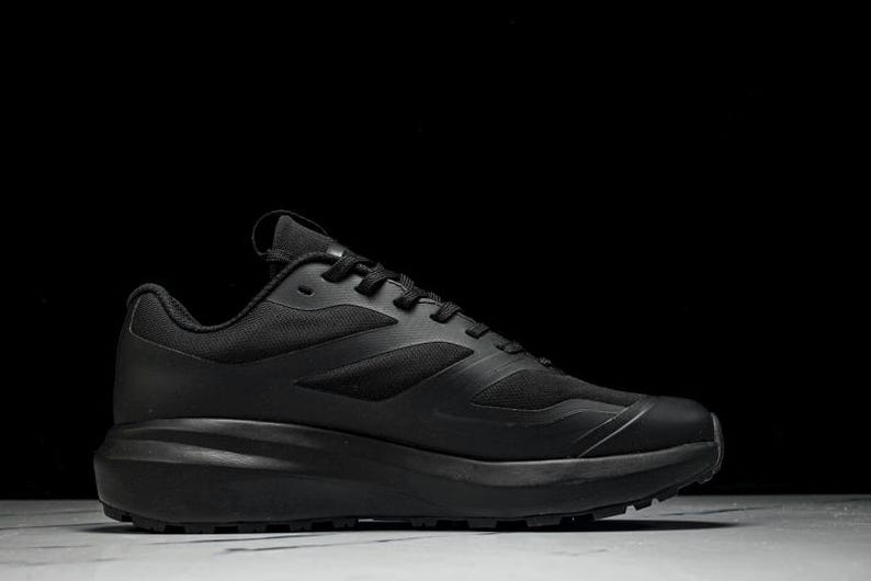 May include: All-black athletic shoe with a thick sole. The shoe features a mesh upper and a textured design. The laces and sole are also black. The shoe is designed for running or other athletic activities.