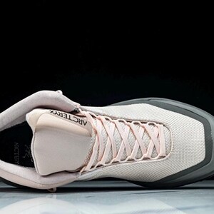 May include: A light pink and gray athletic shoe with the brand name "Arc'teryx" visible. The shoe has light pink laces and a gray sole. The shoe is designed for athletic activities.