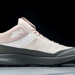 May include: A modern athletic shoe in a neutral color palette. The shoe features a light pink collar and tongue, a white midsection, and a gray base and sole. The design is sleek and contemporary, suitable for various activities.