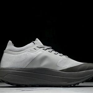 Puede incluir: Una zapatilla deportiva gris con suela gris oscuro y parte superior gris claro. La zapatilla tiene un dise&ntilde;o de malla texturizada en los laterales y un cuello acolchado. Los cordones son grises, sobre un fondo negro.