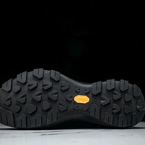 Puede incluir: Suela de bota de senderismo negra con un patr&oacute;n texturizado para agarre. La suela presenta un prominente logotipo naranja "Vibram", que indica la marca y la calidad del calzado. El dise&ntilde;o sugiere durabilidad y tracci&oacute;n.