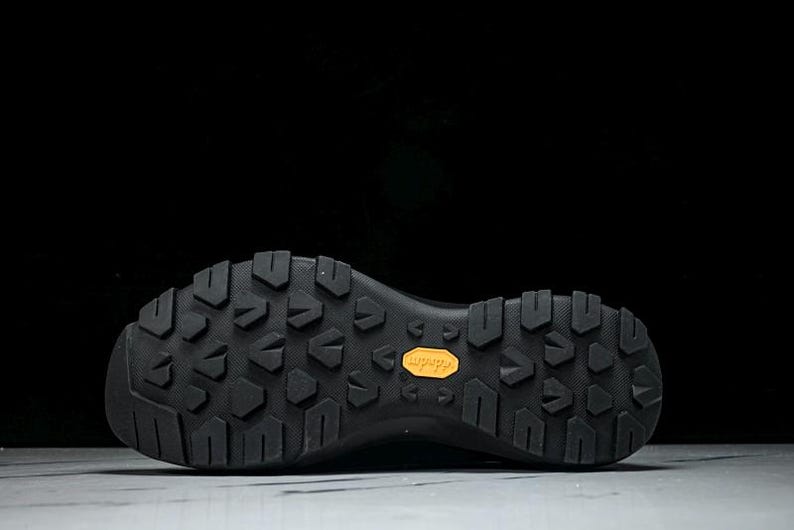 Puede incluir: Suela de bota de senderismo negra con un patr&oacute;n texturizado para agarre. La suela presenta un prominente logotipo naranja "Vibram", que indica la marca y la calidad del calzado. El dise&ntilde;o sugiere durabilidad y tracci&oacute;n.