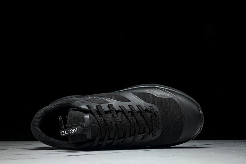 May include: A black athletic shoe with black laces and a mesh upper. The shoe is lying on its side, with the sole facing up. The word "ARCTERYX" is visible on the shoe's tongue.