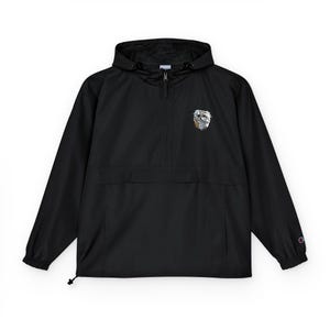 May include: Black anorak jacket with a hood and a half-zip closure. The jacket features a small, colorful graphic on the chest and a Champion logo on the sleeve. The anorak has a drawstring at the bottom and elastic cuffs.