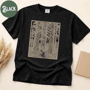 Może przedstawiać: Czarny t-shirt z kr&oacute;tkim rękawem z prostokątnym nadrukiem graficznym przedstawiającym scenę leśną z wysokimi drzewami i krętą ścieżką w jasnobrązowym kolorze. Koszulka ma okrągły dekolt i metkę marki Comfort Colors na wewnętrznym kołnierzu.