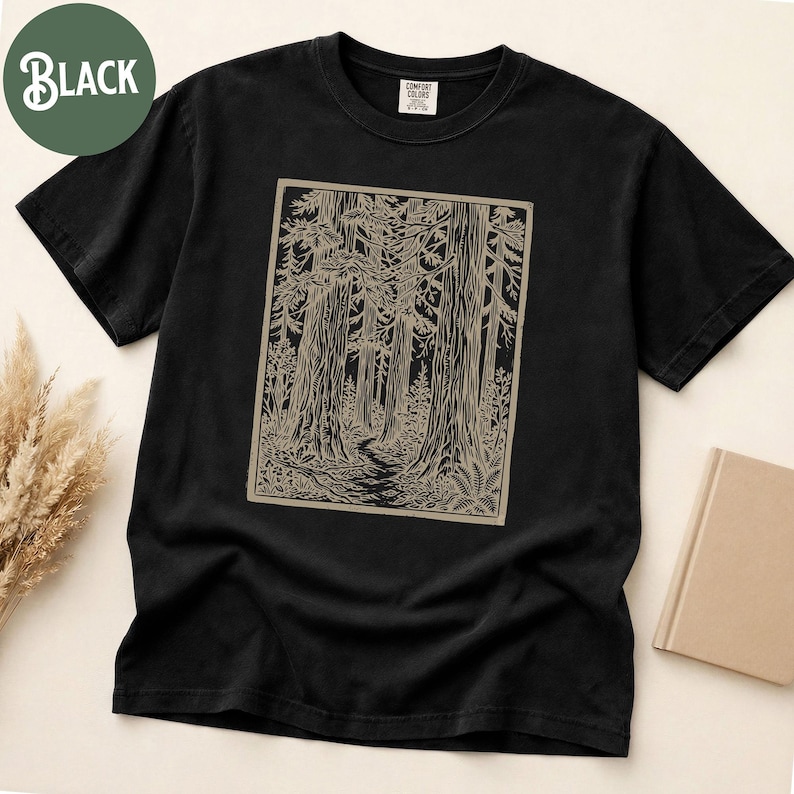 Może przedstawiać: Czarny t-shirt z kr&oacute;tkim rękawem z prostokątnym nadrukiem graficznym przedstawiającym scenę leśną z wysokimi drzewami i krętą ścieżką w jasnobrązowym kolorze. Koszulka ma okrągły dekolt i metkę marki Comfort Colors na wewnętrznym kołnierzu.