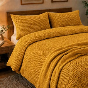 May include: A mustard yellow bedding set featuring a textured waffle weave pattern. The set includes a duvet cover and two matching rectangular pillow shams, all displaying a consistent grid-like fabric construction in a deep, warm golden hue.