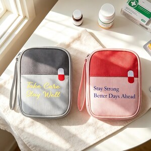 May include: Two rectangular zipped pouches with wrist straps. The left pouch is dark and light grey with the yellow text "Take Care Stay Well". The right pouch is red and light pink with the blue text "Stay Strong Better Days Ahead". Both feature a small pill-shaped graphic.
