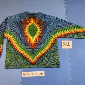 Op de afbeelding: Een 3XL tie-dye shirt met lange mouwen. Het shirt heeft een levendig patroon met een centraal diamantontwerp in groen, oranje en geel, omgeven door blauwe en groene tinten. De tekst "TieDyeSteve.com" is zichtbaar.