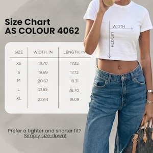 以下が含まれることがあります： AS Colour 4062のサイズチャートが付いた白いクロップトップ。XSからXLまでのサイズの寸法をセンチメートルで表示。テキスト「Prefer a tighter and shorter fit? Simply size down!」も含まれています。