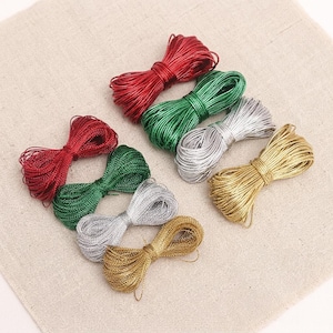 May include: A collection of seven small bundles of metallic cord arranged in two rows. The bundles are colored in red, green, silver, and gold. Each bundle is tied in the center, creating a bow-like shape with a shiny, reflective texture.