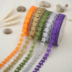 May include: A selection of decorative leaf-patterned ribbon in a range of colours, including orange, beige, green, grey, and purple. This ribbon is suitable for craft projects and adding embellishments. The ribbon is sold on a spool.