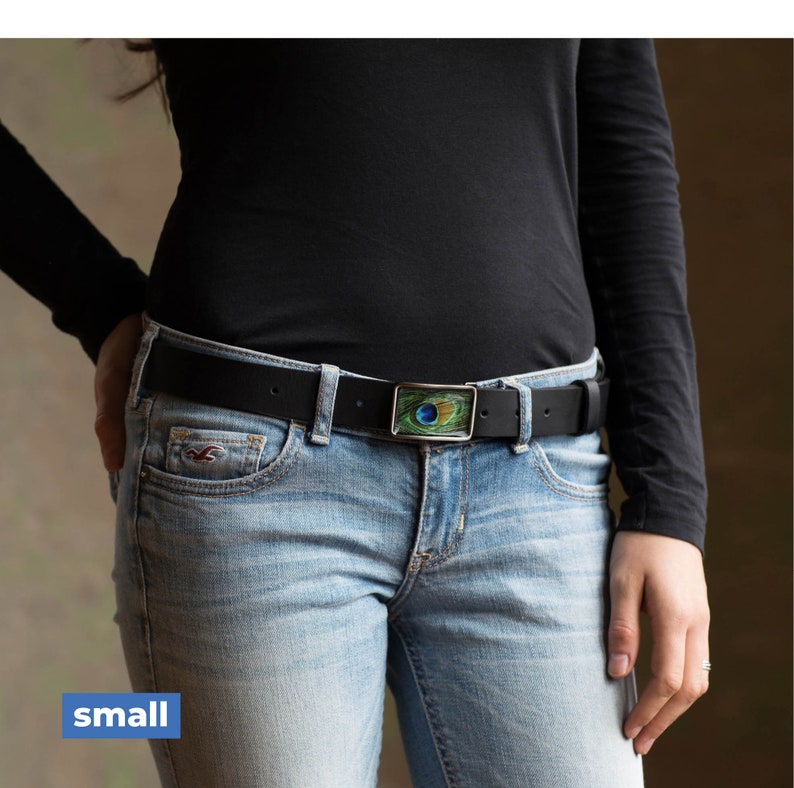 Peut inclure: Une ceinture en cuir noir avec une boucle argent&eacute;e orn&eacute;e d'un motif de plume de paon. La boucle est rectangulaire et pr&eacute;sente un motif de plume de paon vert, bleu et or.
