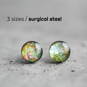 May include: A pair of small, round earrings with a floral pattern. The earrings are made of surgical steel and have a silver finish.