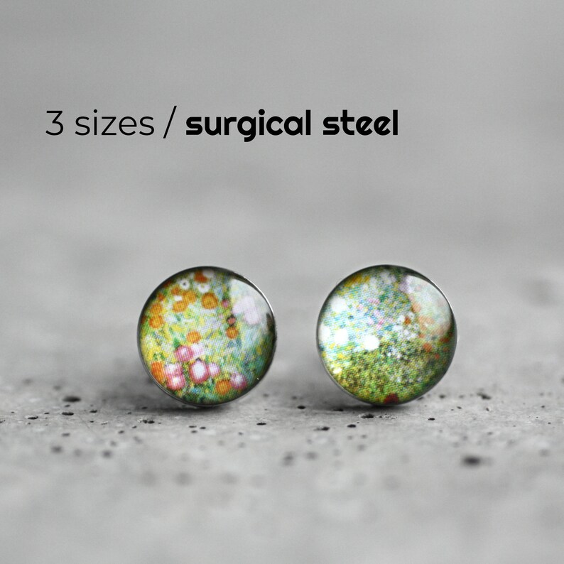 May include: A pair of small, round earrings with a floral pattern. The earrings are made of surgical steel and have a silver finish.