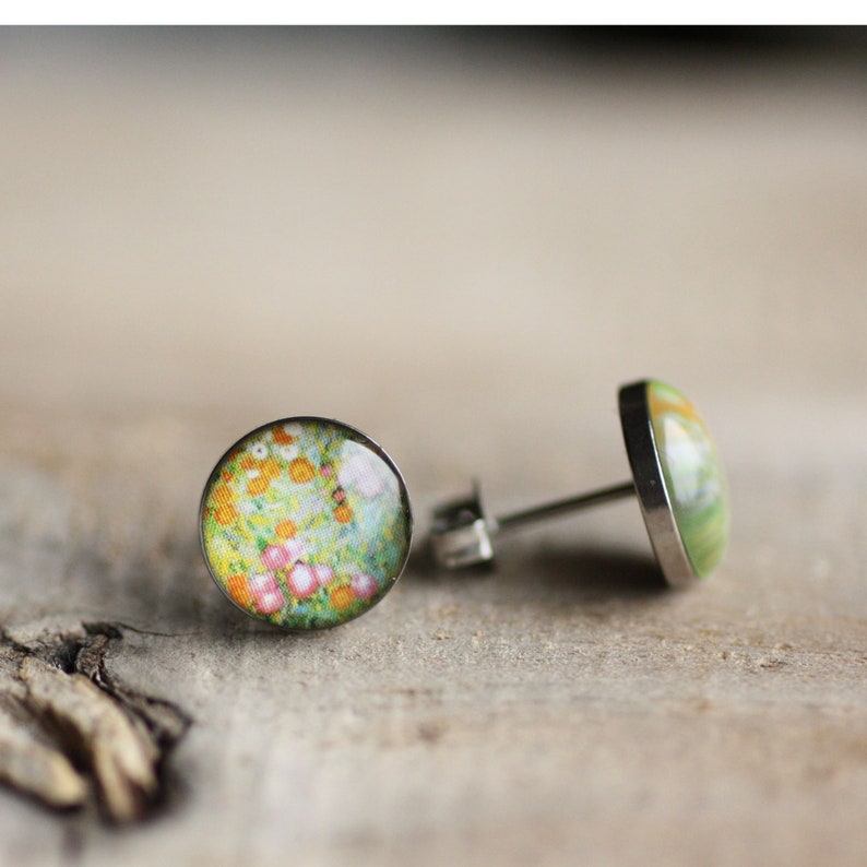 May include: A pair of silver stud earrings with a floral pattern in shades of yellow, green, pink, and white.