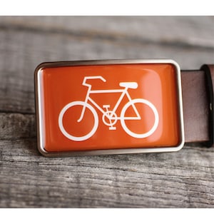 Peut inclure: Une boucle de ceinture argent&eacute;e avec un fond orange et une silhouette blanche d'un v&eacute;lo.