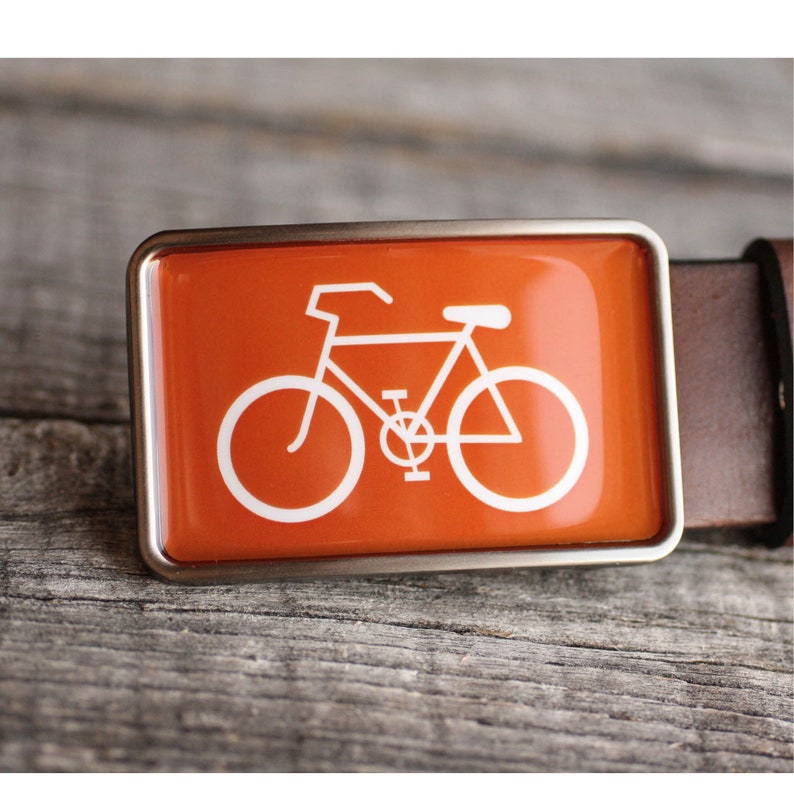 Peut inclure: Une boucle de ceinture argent&eacute;e avec un fond orange et une silhouette blanche d'un v&eacute;lo.
