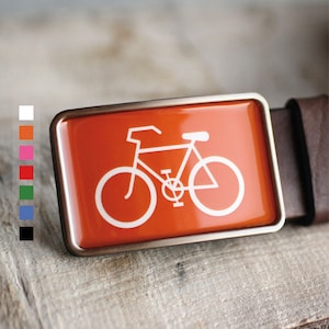 Peut inclure: Une boucle de ceinture argent&eacute;e avec un fond orange vif et une silhouette blanche d'un v&eacute;lo.