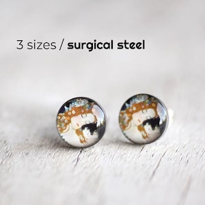 May include: A pair of silver stud earrings with a round, colorful image of a woman's face. The earrings are made of surgical steel. 3 sizes / surgical steel