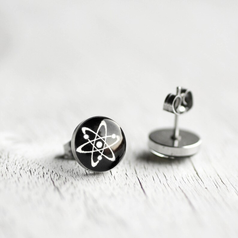 Pu&ograve; includere: Un paio di orecchini a perno d'argento con un design circolare nero che presenta un simbolo di atomo bianco.