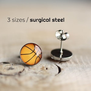 May include: A pair of basketball-themed earrings with orange and black details. The earrings are made of surgical steel and have a post back.