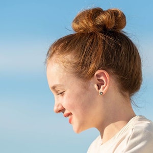 Pu&ograve; includere: Una ragazza giovane con i capelli rossi raccolti in uno chignon, indossa una camicia bianca e sorride guardando in basso.