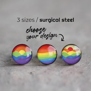 May include: Three round stud earrings with a rainbow design. The earrings feature a vibrant spectrum of colors, including red, orange, yellow, green, blue, and purple. The text "3 sizes / surgical steel choose your design" is above the earrings.
